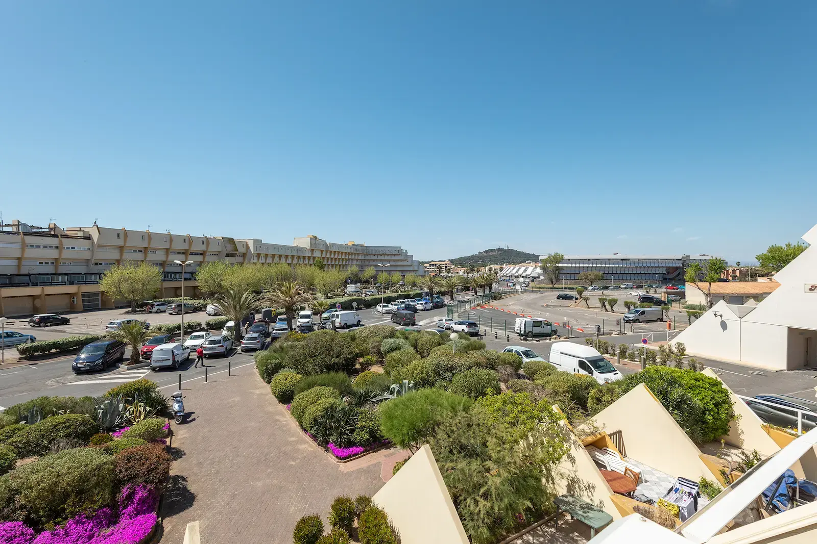 Panoramic view of the Village Naturiste district of Cap d’Agde with parking lots, residences, Mediterranean vegetation and hills in the background under a clear sky